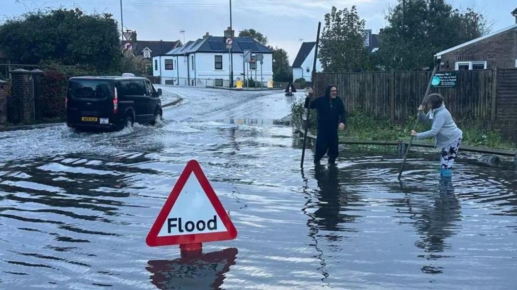 Two people stand in floodwater in London Road, Bognor Regis, West Sussex, 