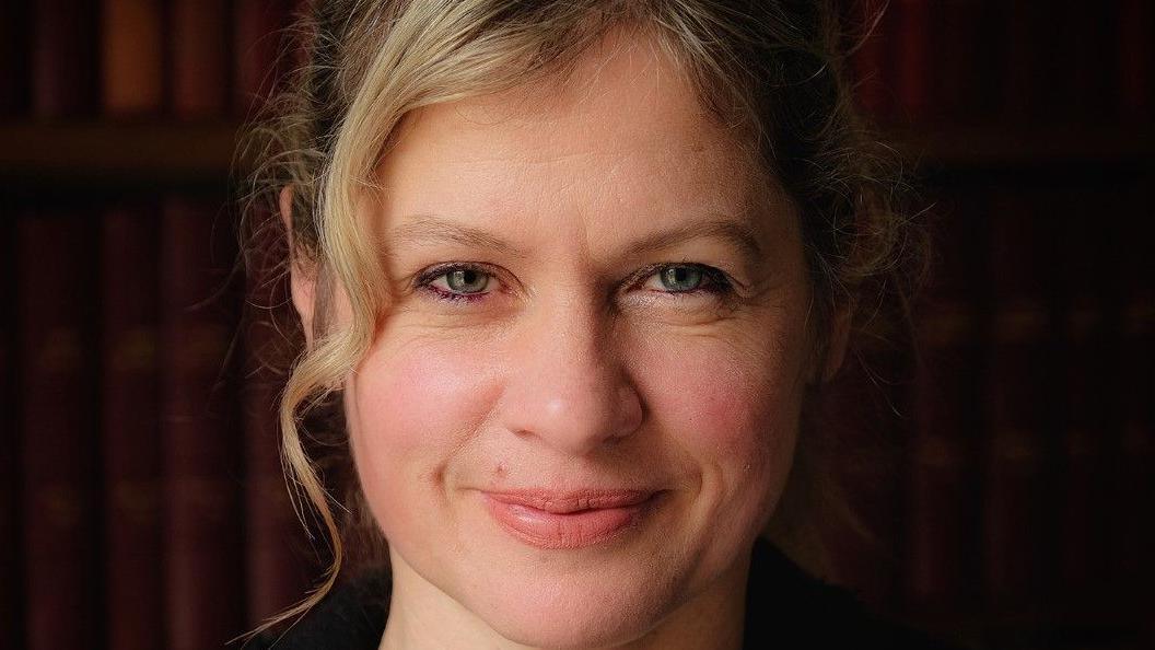 Headshot of Hilary Pullum, who has dark blonde hair that has been tied up and hazel-coloured eyes.
