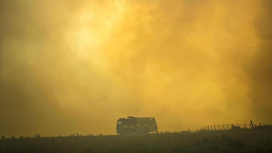 The silhouette of a fire engine is visible against a yellow haze as smoke fills the air.