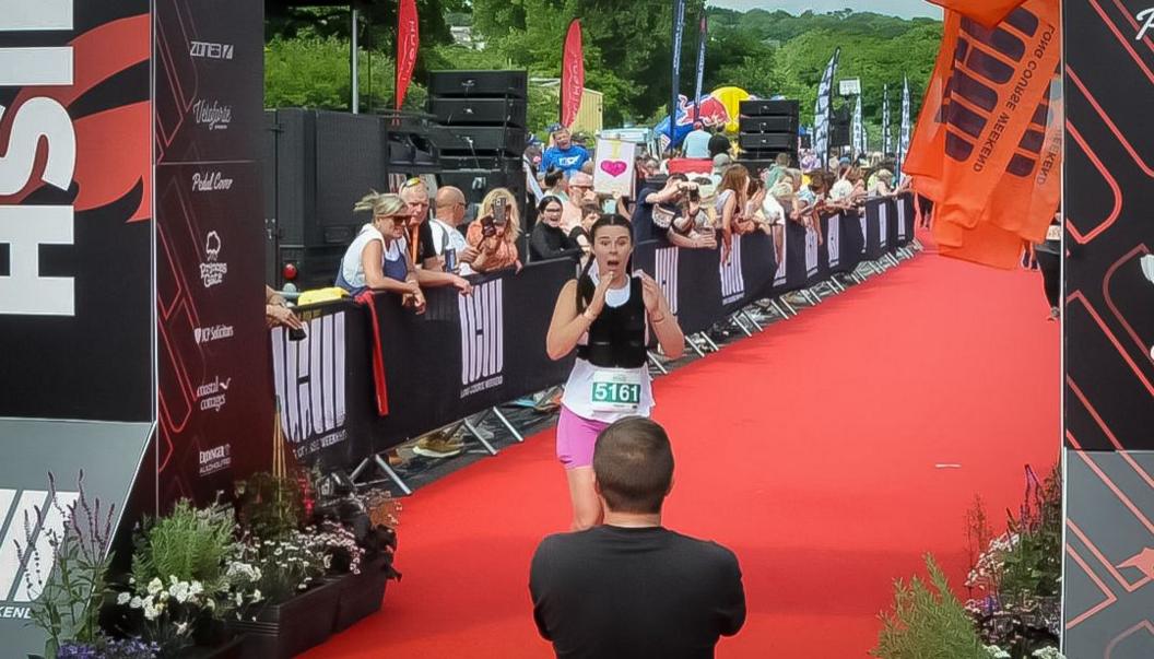 Thomas down on one knee at the finish line where Sarah hold her hands to her mouth in shock 