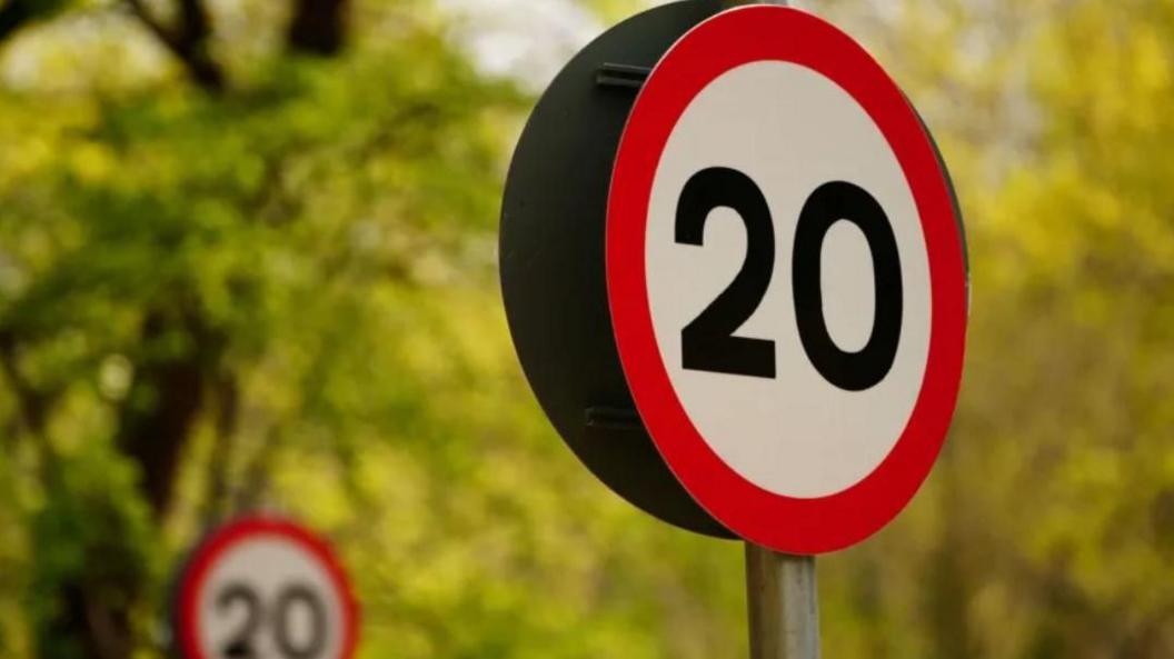 A red and white 20 miles per hour traffic sign, with another blurred in the background.