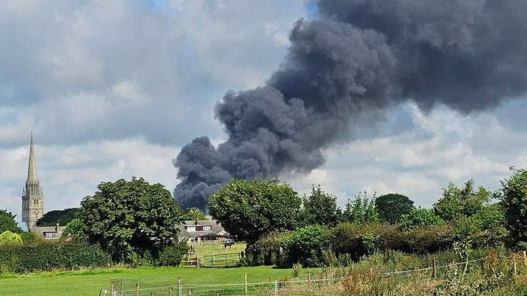 Smoke fills the sky in Patrington, with a church to the left of the blaze and houses and gardens to the front