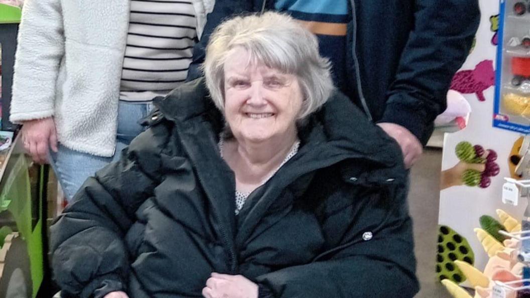 Mary Marlow smiles in a wheelchair wearing black puffer jacket