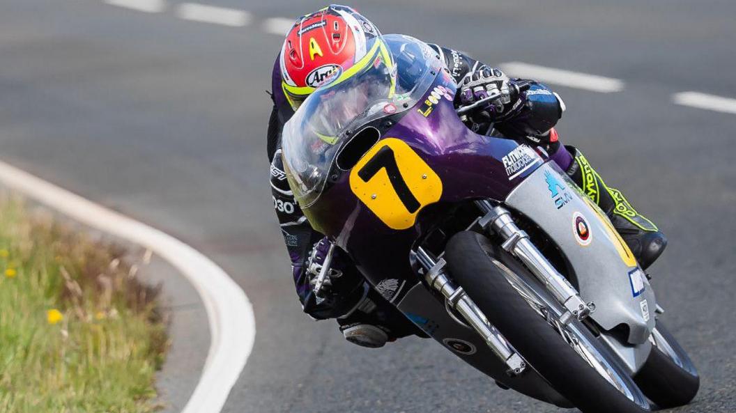 Adam McLean, on a silver and purple machine with the number seven in the front. His helmet is red, yellow and white.