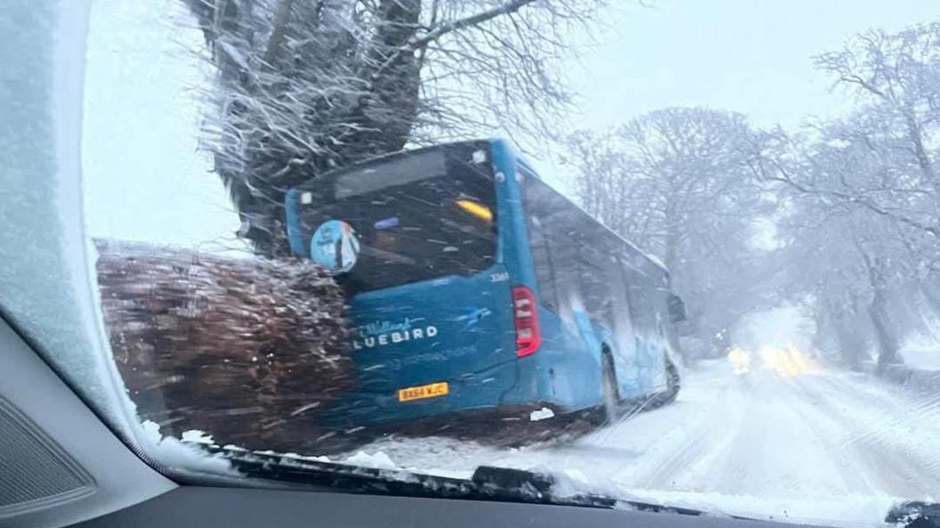 A blue bus is tilted to the side after going off the road. The photo is taken through a car windscreen.