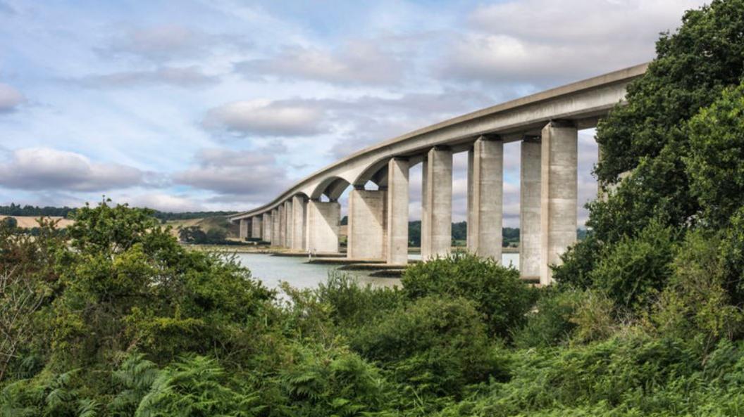 The Orwell Bridge seen from the northern bank looking across the river towards Wherstead. The bridge is an arched concrete structure with piers supporting the road.