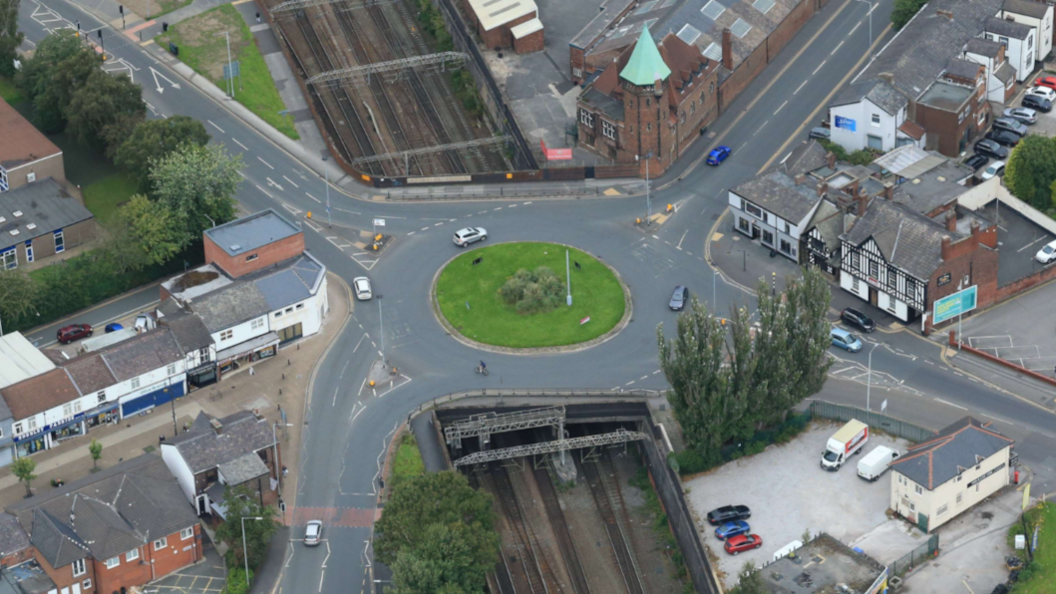 An aerial view of a bridge running underneath a large roundabout which has four roads coming out of it.