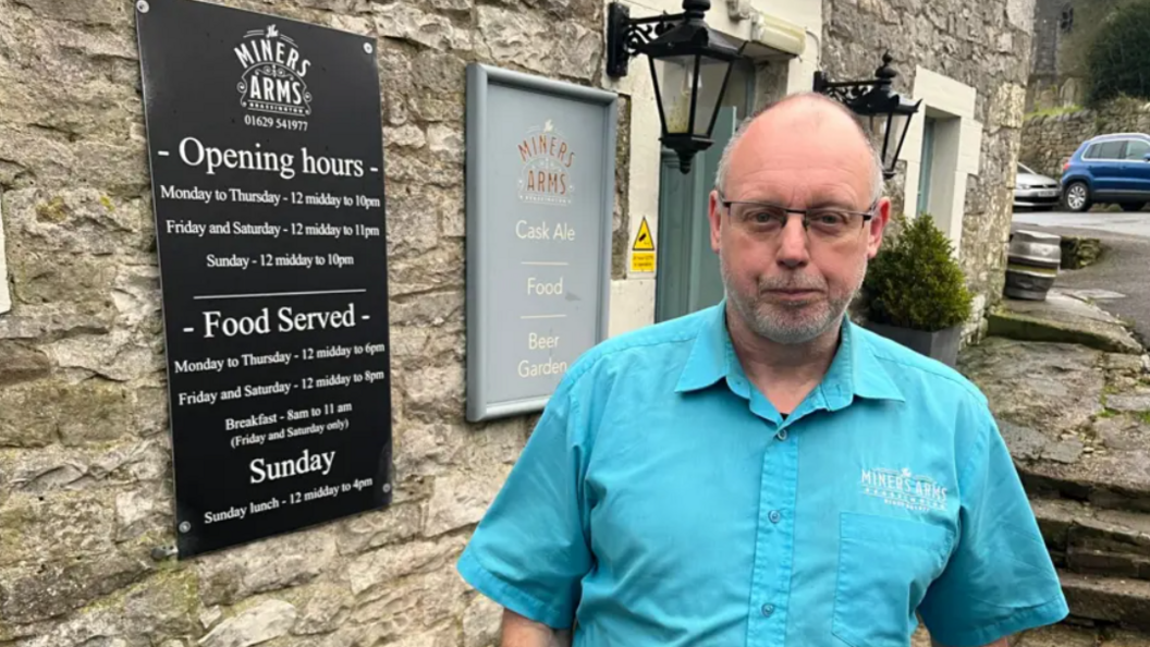 A bald man wearing a blue shirt stood outside of a pub