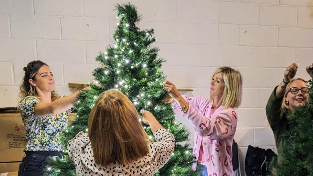 Four women decorating a Christmas tree with lights on it