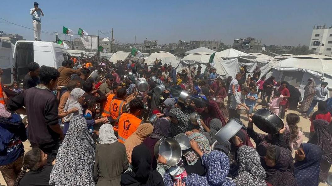 Palestinian women carrying pots scramble to get hot meals at a community kitchen in Jabalia, northern Gaza