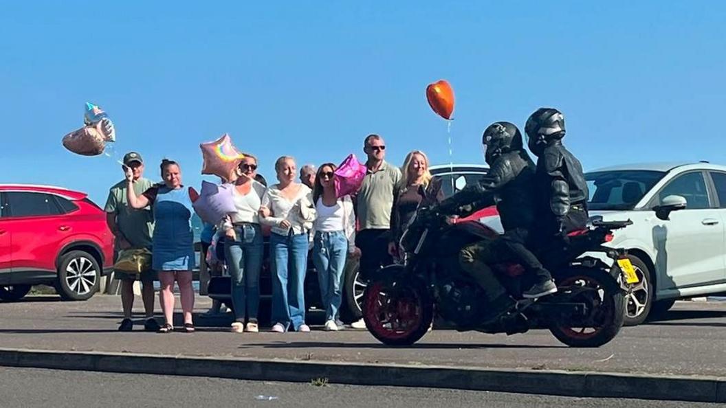 A biker rides past a group of people, a red balloon is flying in the background