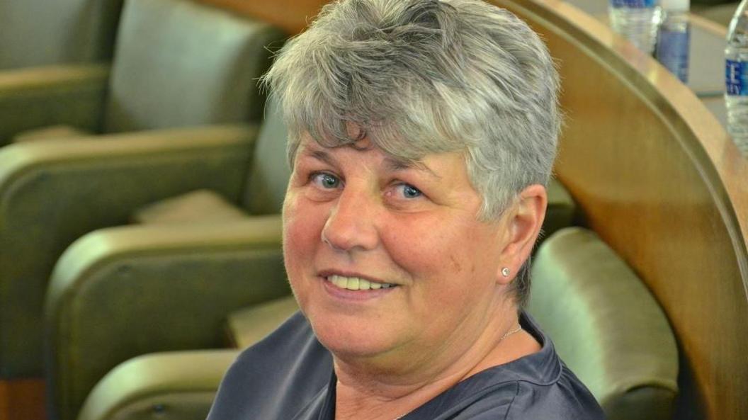 West Lancashire Borough Council leader Yvonne Gagen with short grey hair, blue eyes, wearing a grey top smiling as she sits on a green leather seat