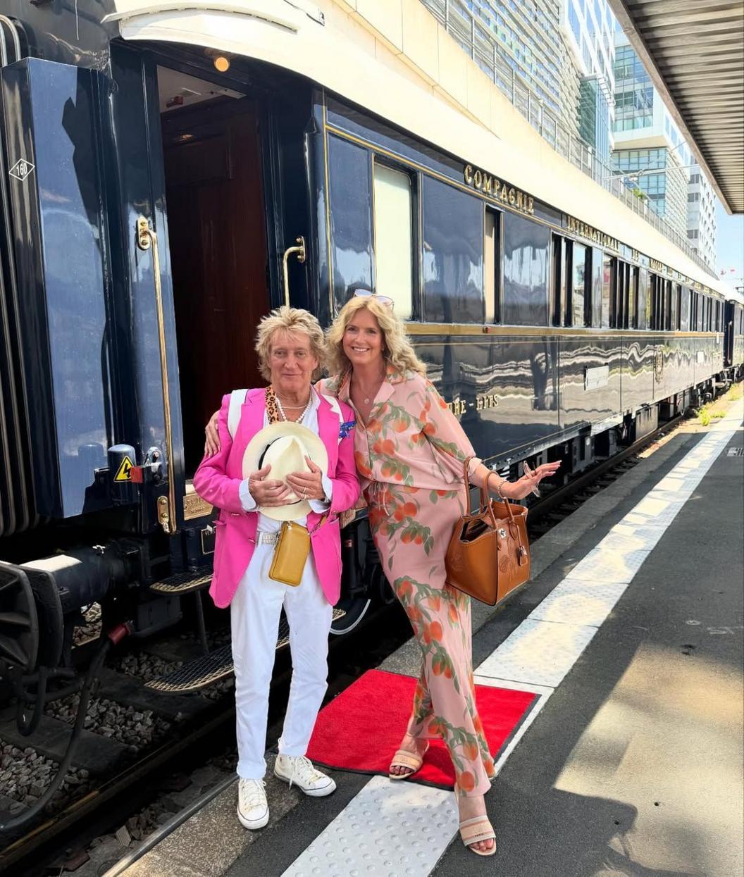 Penny Lancaster hugs her husband Rod Stewart, as they pose outside the Orient Express at a train station.