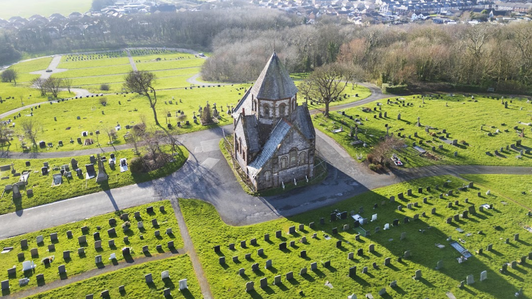 A chapel in Barrow Cemetery looking from above on a sunny day. There are hundreds of graves placed with bright green grass.