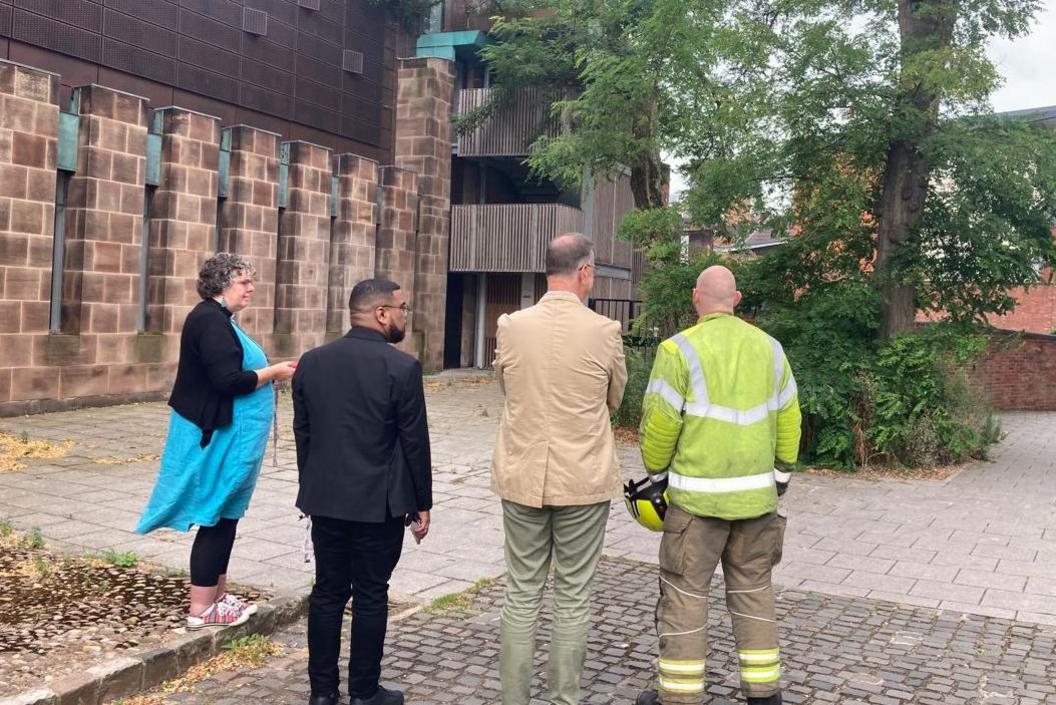 One woman and three men standing and facing towards the fallen tree and cathedral