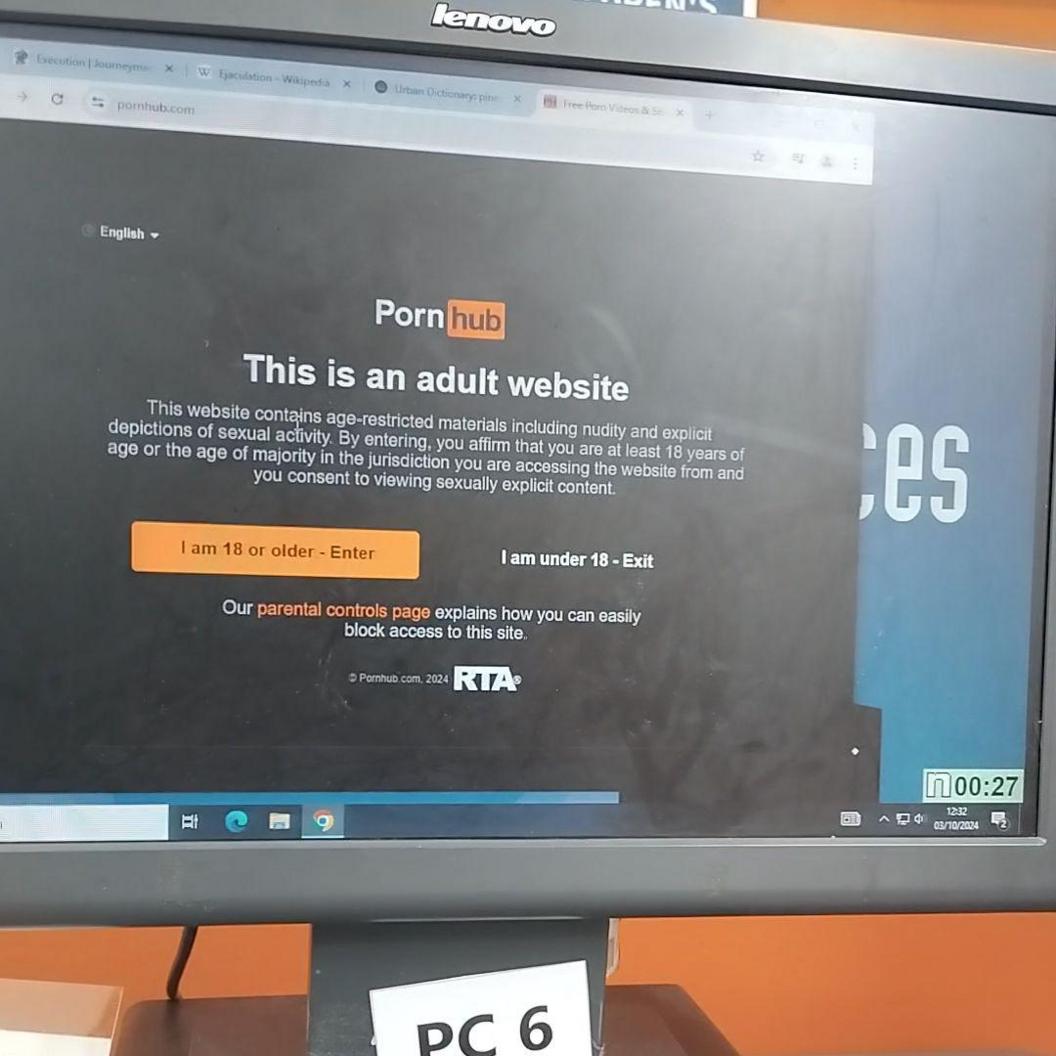 A PC screen located in a library in Edinburgh displaying the pornographic website PornHub's age verification page, which includes white and orange writing on a black background.