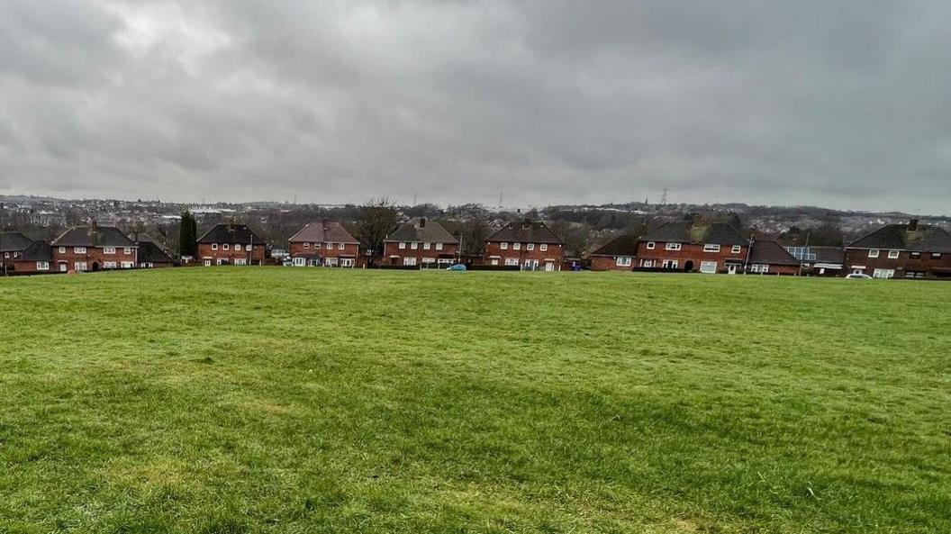 A row of semi-detached houses can be seen with a large open space in front of them.