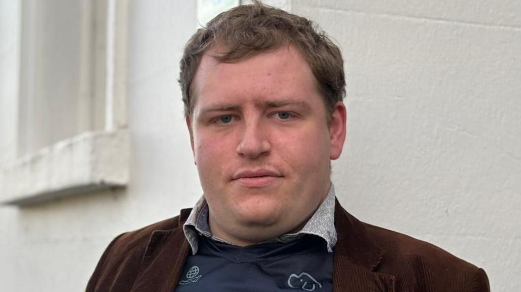 A man standing outside with his "Microsoft Excel World Championship" t-shirt showing underneath his brown jacket