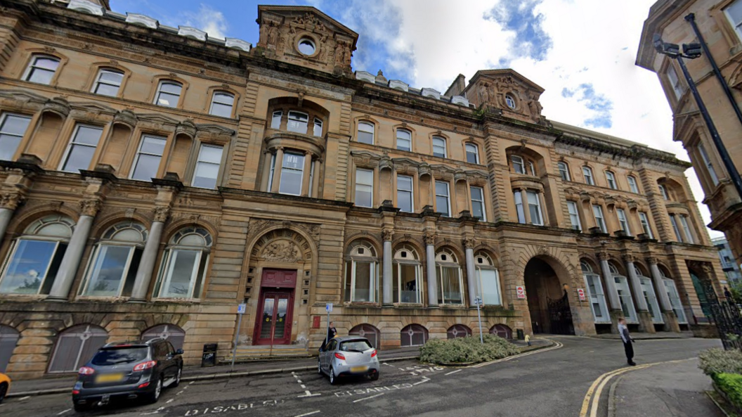 An exterior shot of Inverclyde Council buildings in Greenock with cars parked outside and shrubbery in the foreground.