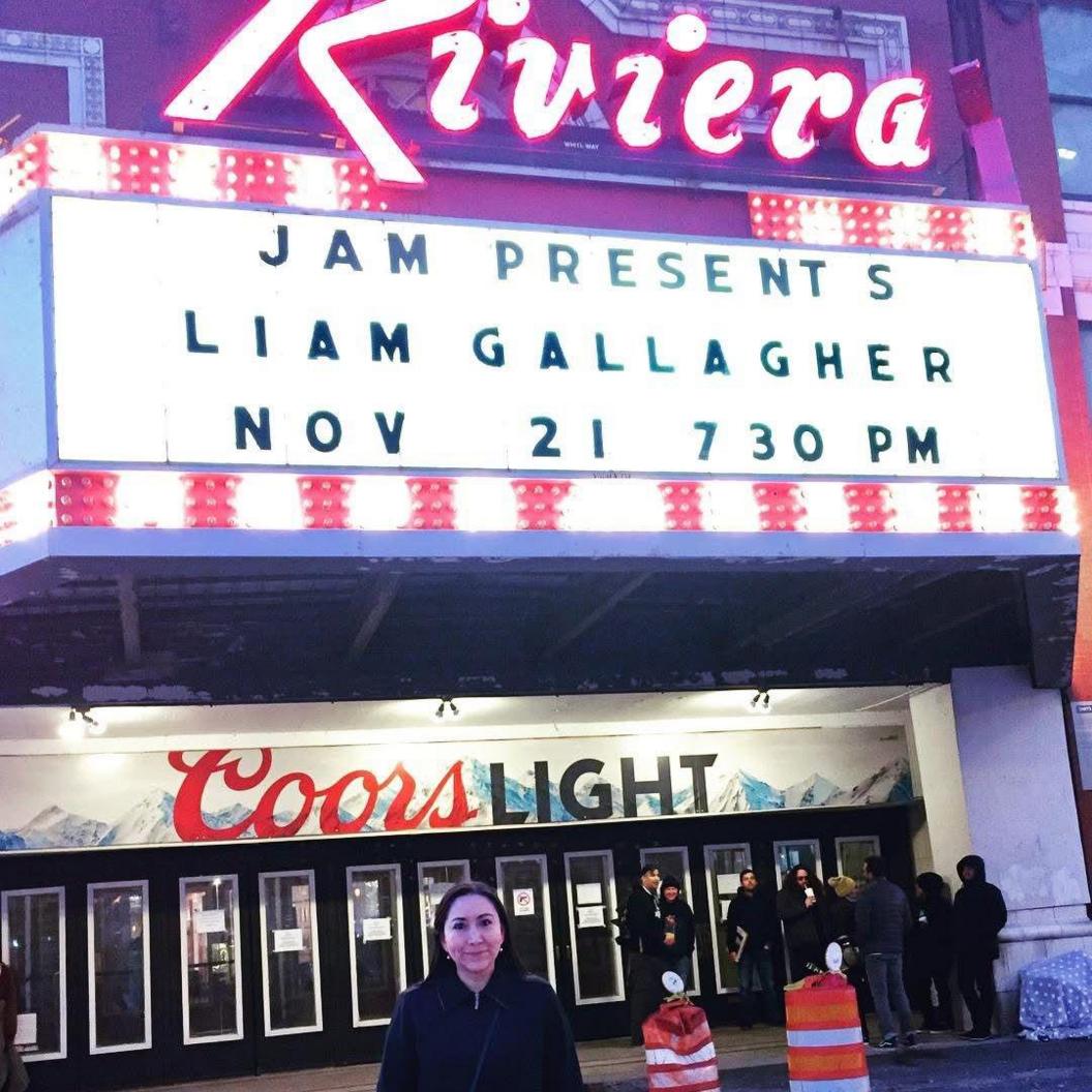Diana Vesely standing in front of a concert venue in Chicago - a large Coors Light advert is behind her, above the entry doors and 'Jam presents Liam Gallagher Nov 21 730 PM' is spelled out in black block capitals on a white backlit board. There is a small queue of people outside the venue
