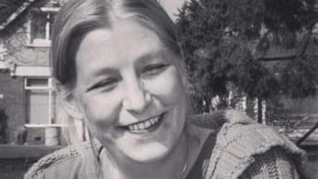 A black and white picture of Dawn Sturgess, smiling at the camera, wearing a knitted cardigan
