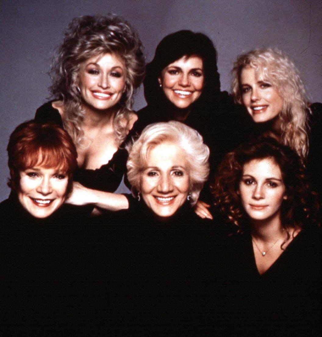 Shirley Maclaine, Dolly Parton, Olympia Dukakis, Sally Field, Julia Roberts and Daryl Hannah smile in a group photo, They all wear black.