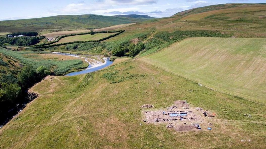 An overhead image of an archaeological dig with a river and hills behind