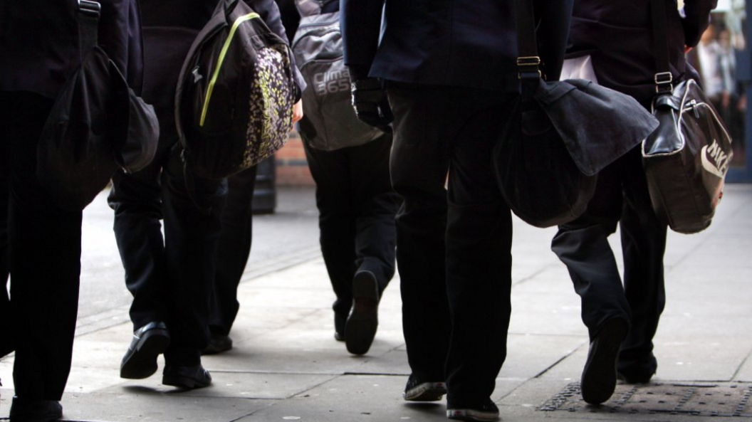 A group in school uniform, carrying bags, are walking away from the camera. None of them can be identified.