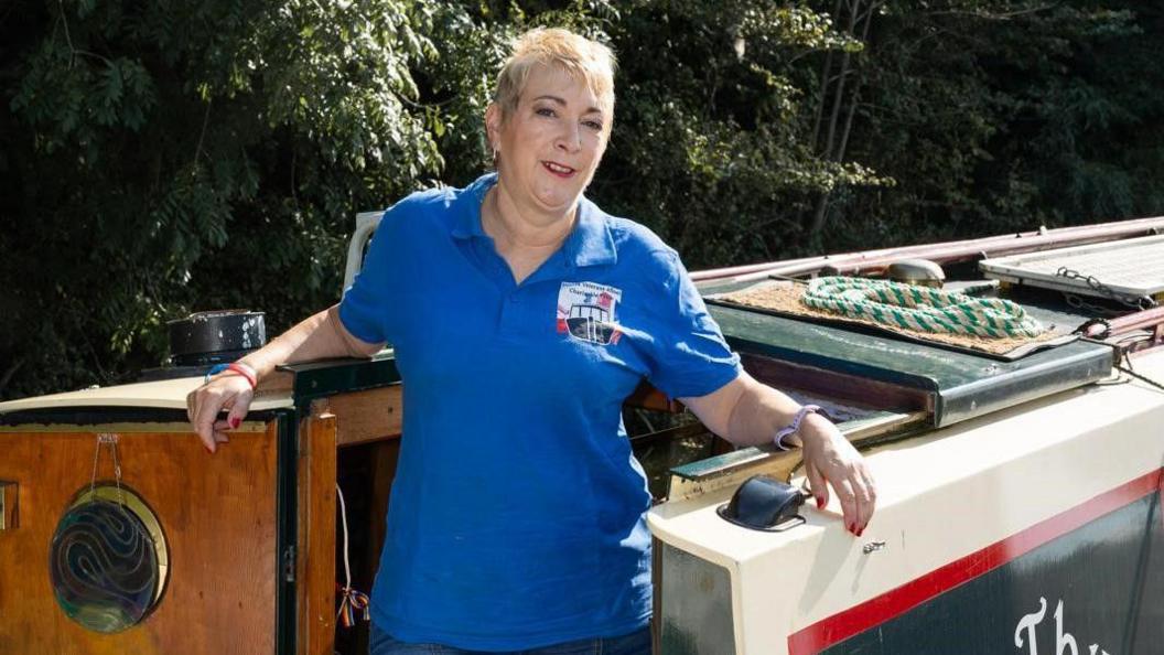 Lizzie Lane, wearing a blue Forces Veterans Afloat polo shirt, standing at the door of her narrowboat