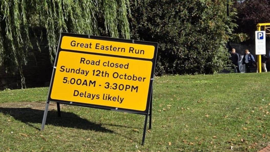 A yellow signboard placed on the grass which says road closed on Sunday, 12 October 