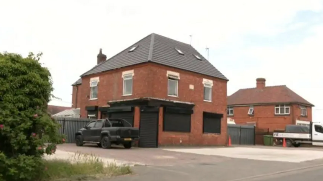 Abattoir site in Arley, Warwickshire. It is a red brick building and the doors and windows have black shutters with a black car parked outside.
