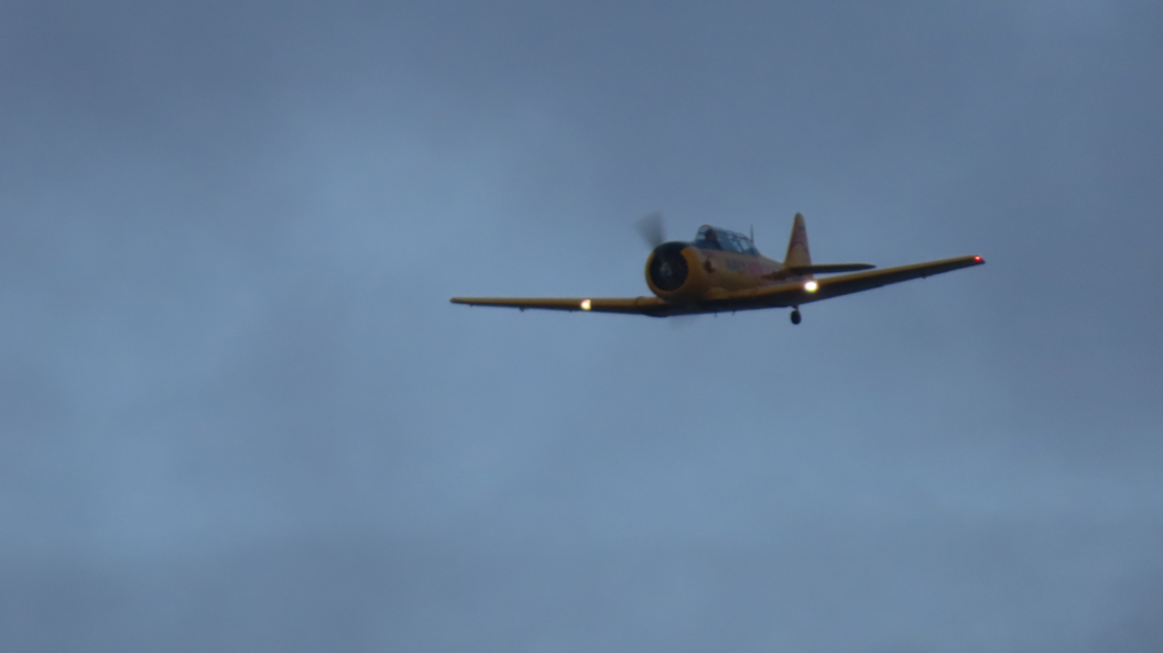A Navy Wings Harvard plane flying upwards in the sky.