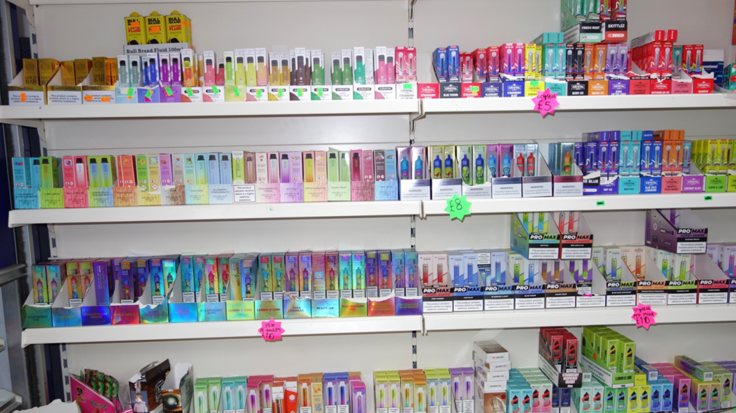 Rows of vapes are on sale in the shop. Four shelves of goods are visible in the image, all different colours with price tags also on display.