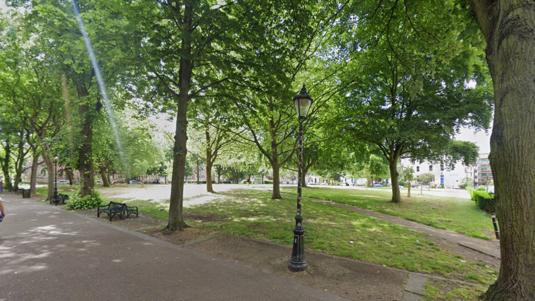 A green space with a number of mature trees and an ornate streetlight next to a pedestrian walkway