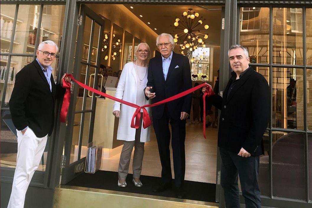 Charlie and his wife stand beside a red ribbon which is held across the door of one of his salons by his sons.