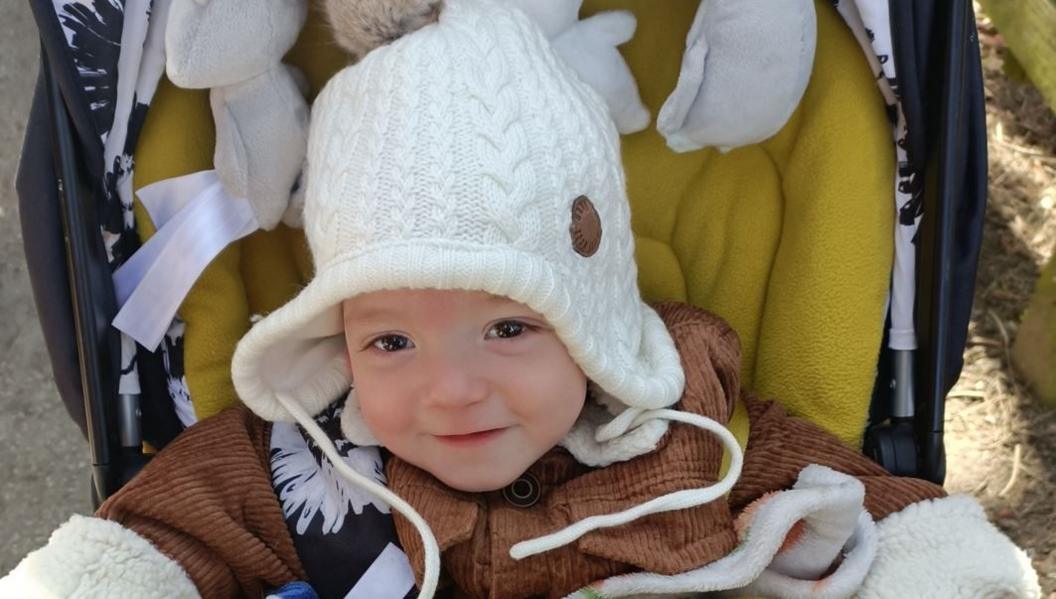 A young boy with large brown eyes wearing a white hat and brown coat looks at the camera.