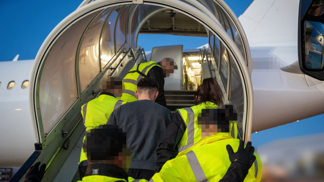 A man being led onto a plane by staff in hi-vis jackets