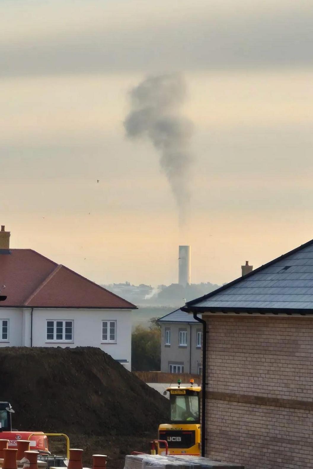 Black smoke rising from a chimney in the distance from a modern housing estate.