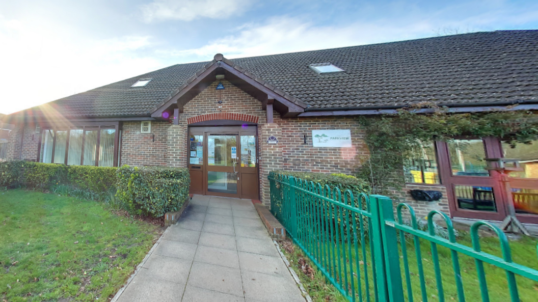 A one-storey building, with hedges in front it with and a green fence on the side.