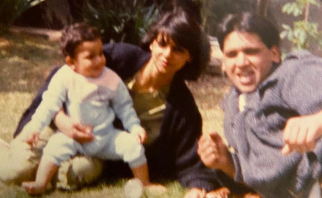 Family picture of two parents and a toddler sitting on the grass smiling at the camera