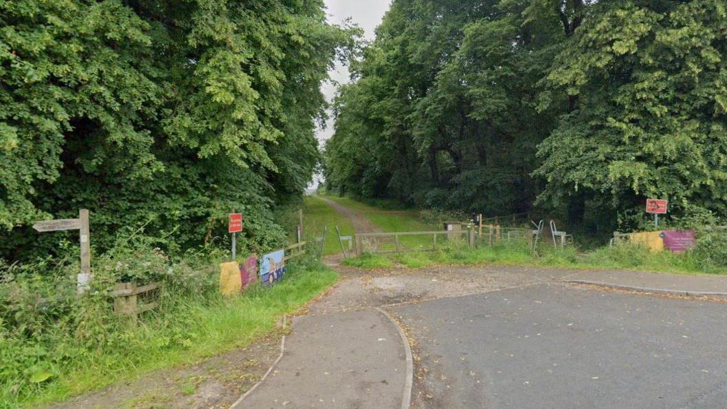 A wooden gate in front of a tree lined path.