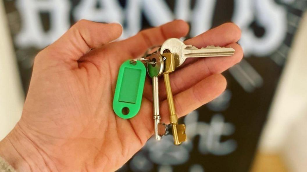 A hand holding a set of keys with a green tag on it and the background is blurred out