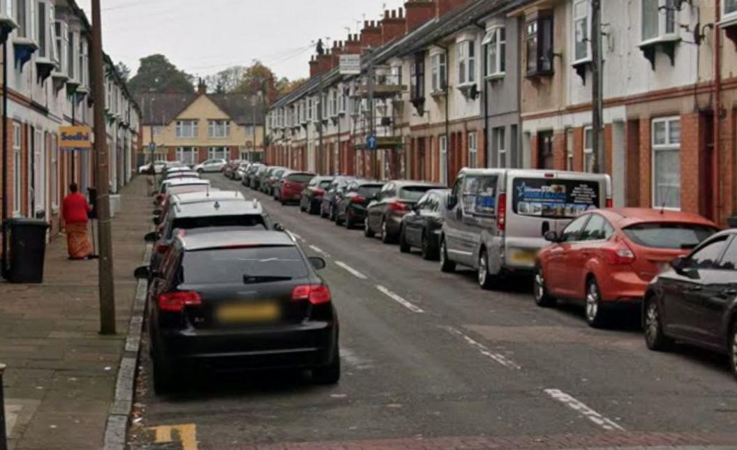 Cars parked on either side of a terraced street, flanked by houses on either side.