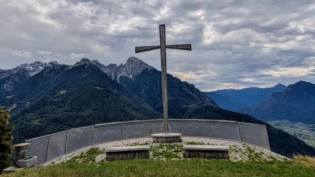 A large cross on top of a raised platform has a grey barrier in front of it. It overlooks several mountain tops on a cloudy day.