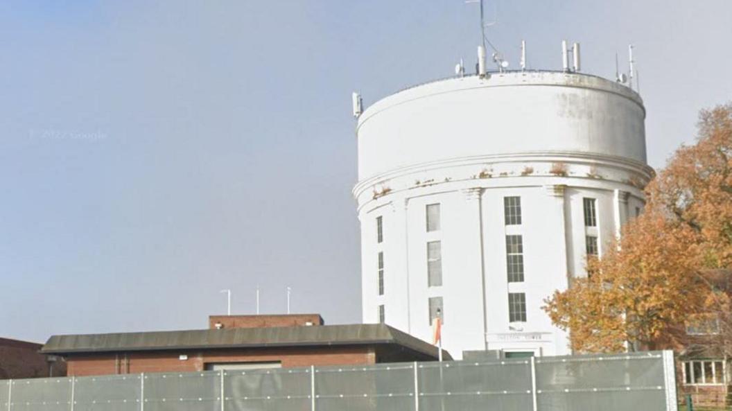 A white cylindrical building behind metal fencing