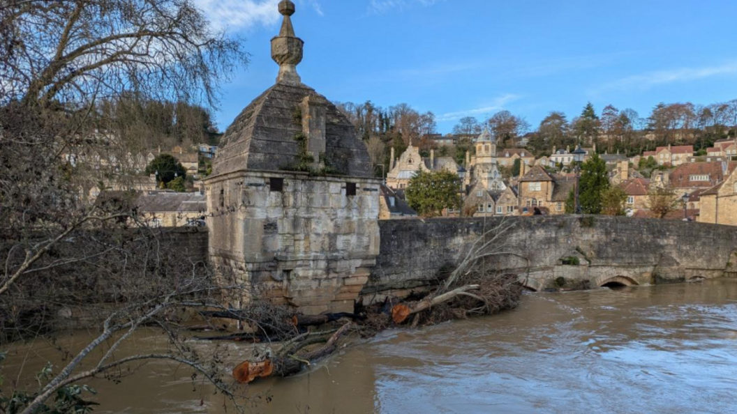 Town Bridge in Bradford-on-Avon with the river level right up to the parapet and a large tree trunk which has been swept down the river and is jammed against the bridge