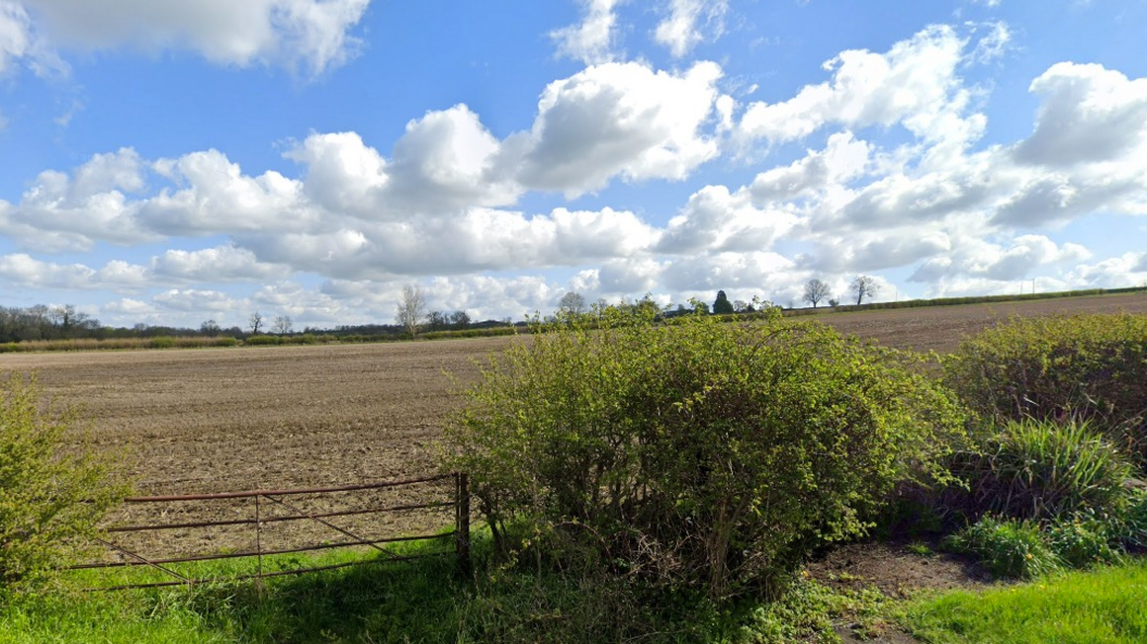 A ploughed field below a blue sky with clouds