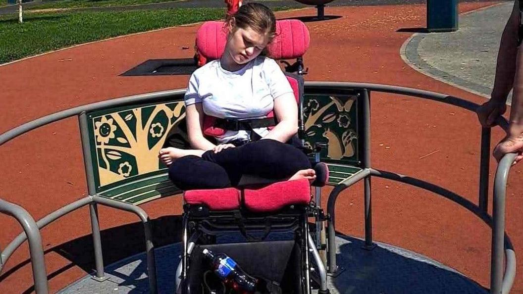 Sianon is in a white T-shirt and navy trousers in her wheelchair.
She is enjoying a wheelchair-accessible ride at the play park in Strathfoyle.
A person out of shot can be seen holding a railing on the ride.