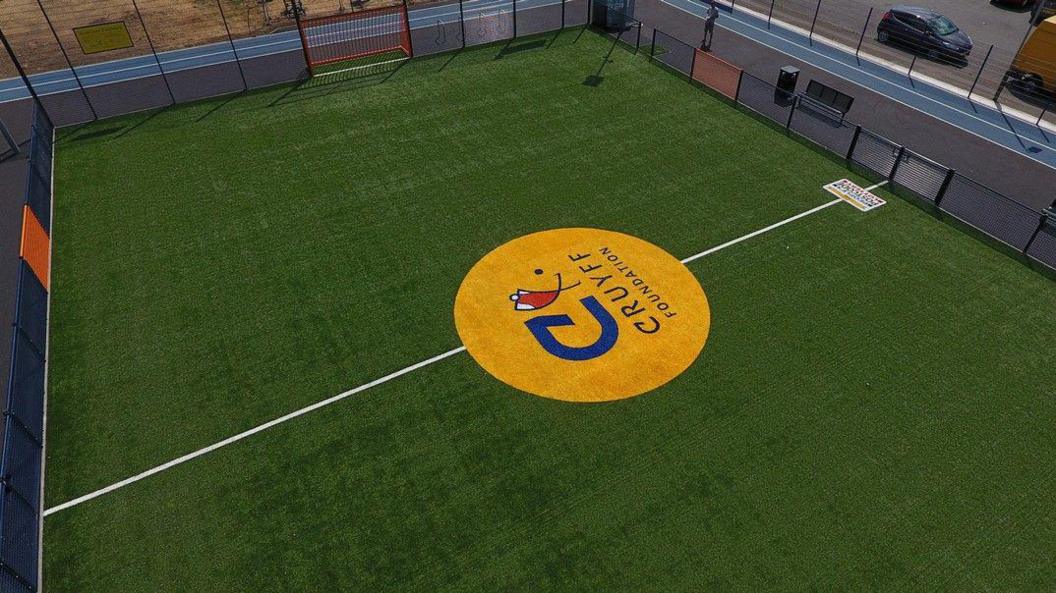 An example of what the new pitch will look like. It is a green all-weather surface with blue and orange fencing around the side.