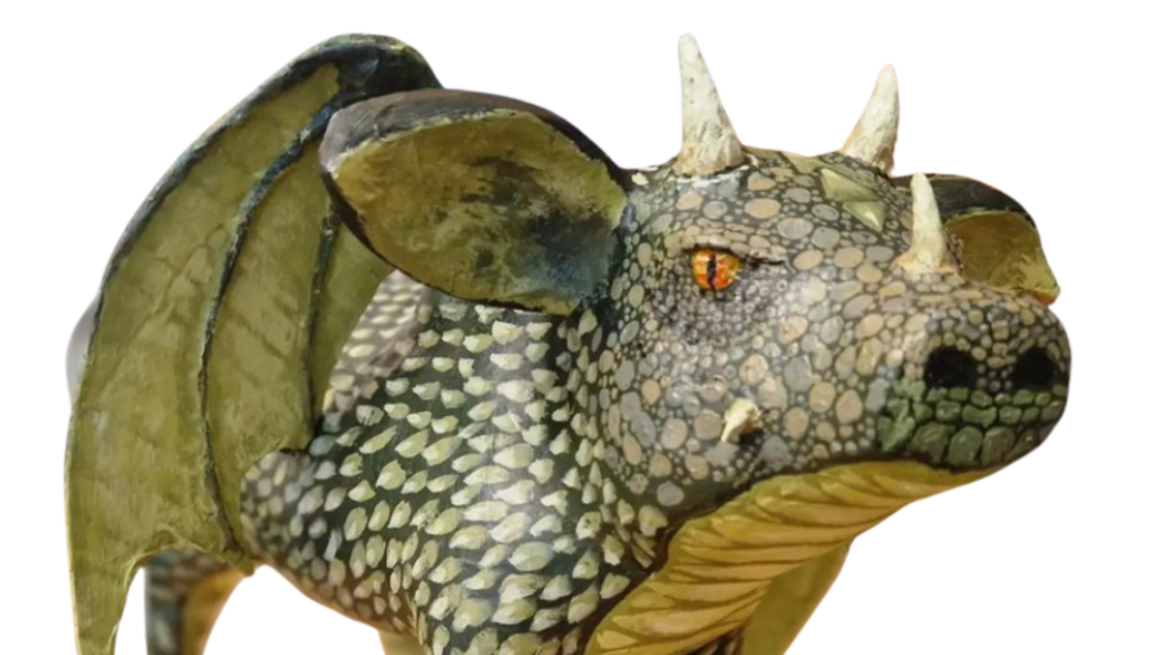 Close-up of model dragon in a slightly pig shape, with painted green scales, lizard-like wings attached and added horns.